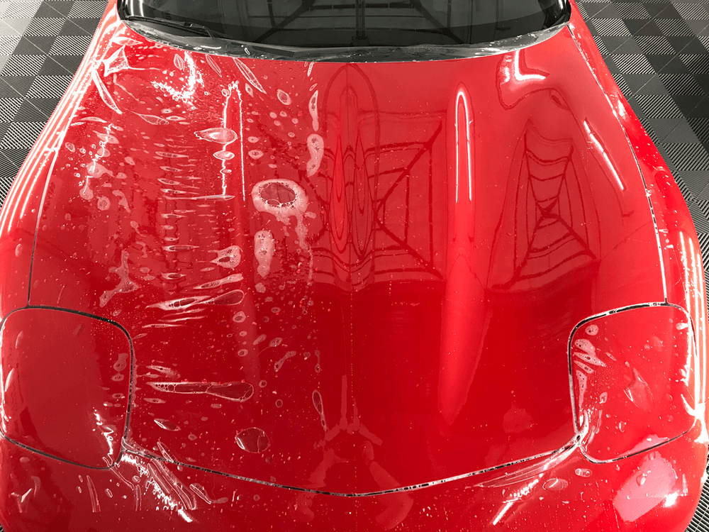 The hood of a red car is covered in plastic.