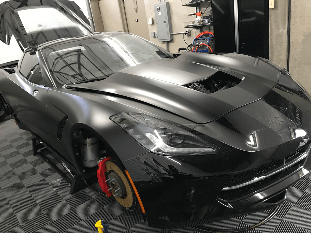 A black sports car with the hood up is parked in a garage.