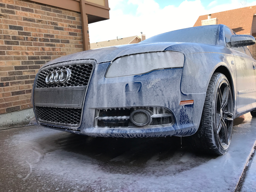 A dirty car is parked in front of a brick building.