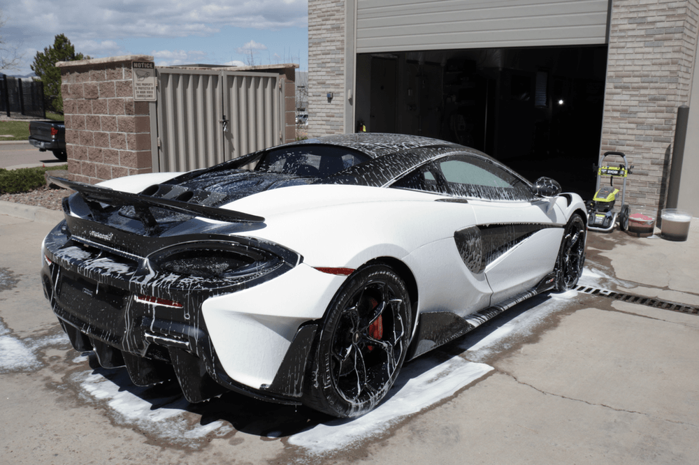 A white sports car is being washed in front of a garage.