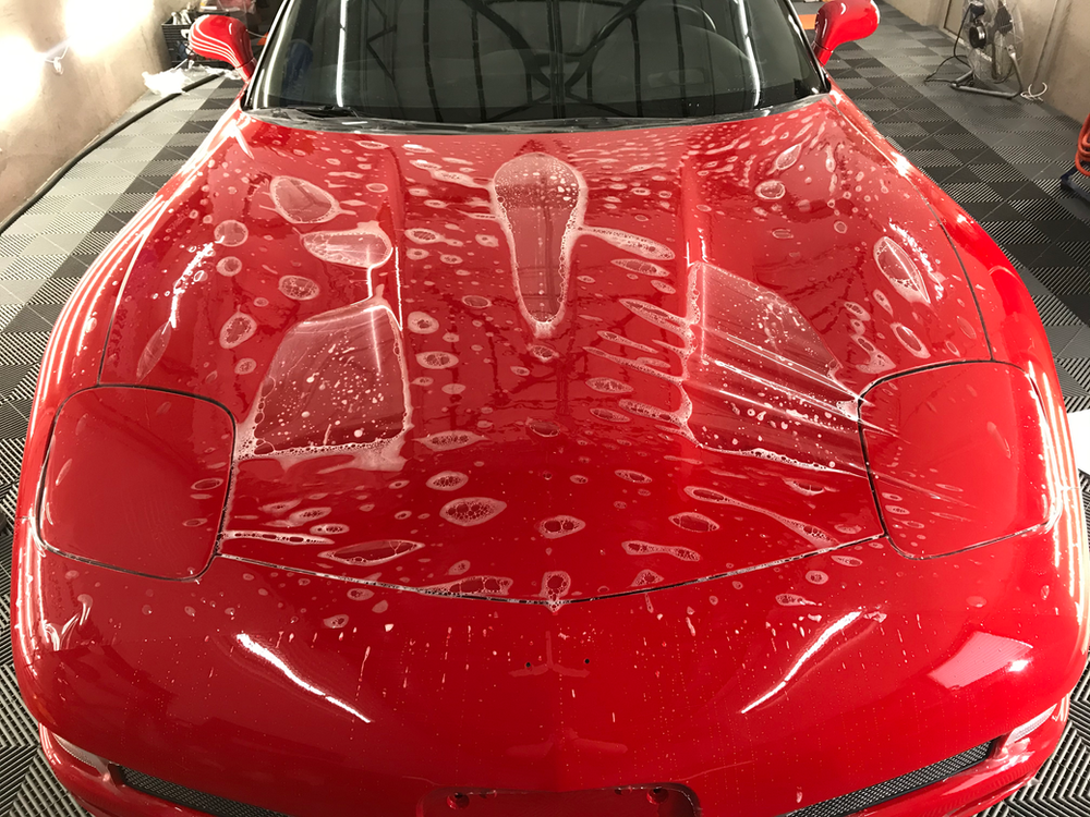 A red car is covered in plastic wrap in a garage.