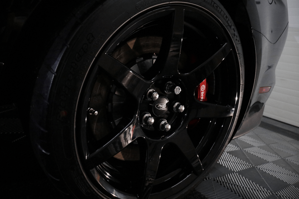 A close up of a black car wheel with a red brake caliper.