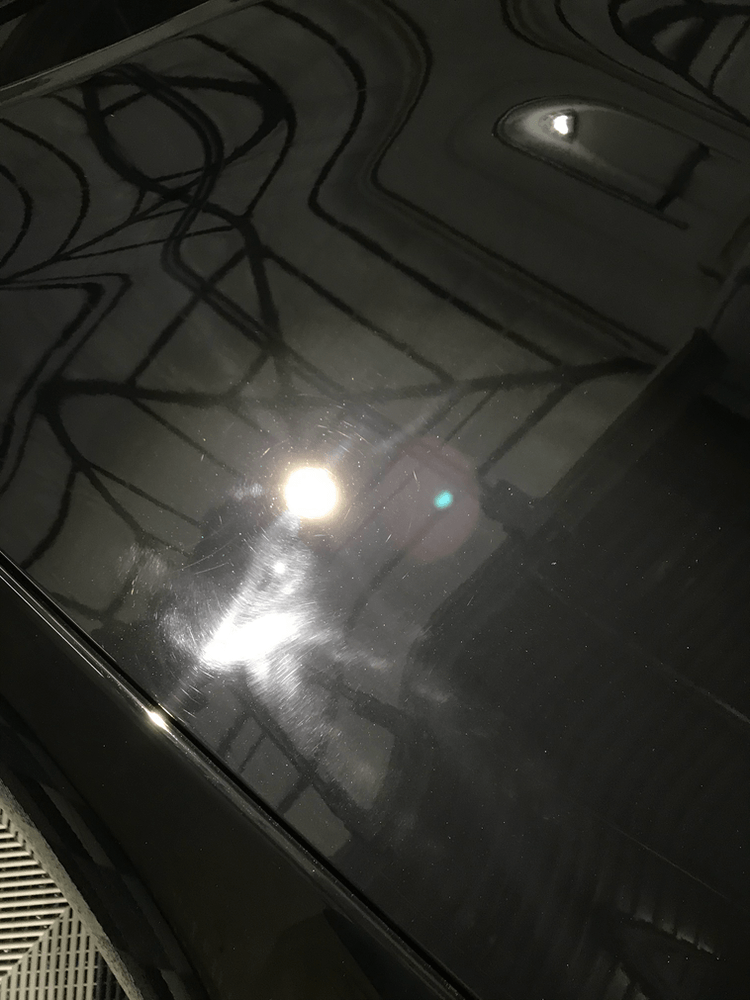 A close up of a black car 's hood with a green light reflected in it.