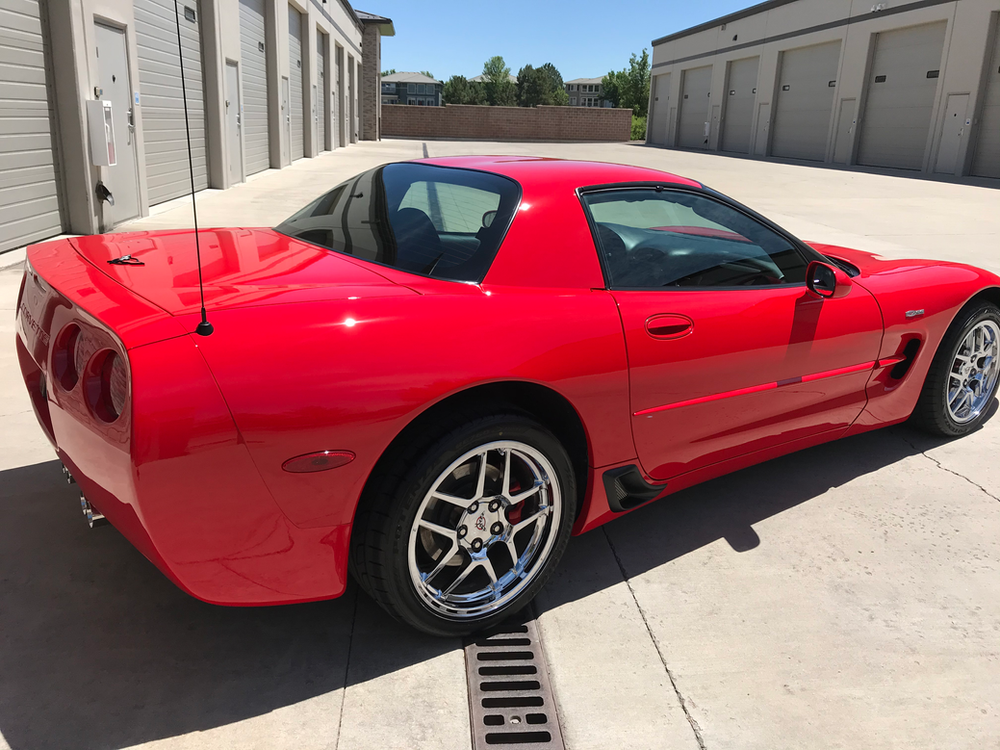 A red corvette is parked in a parking lot next to a building.