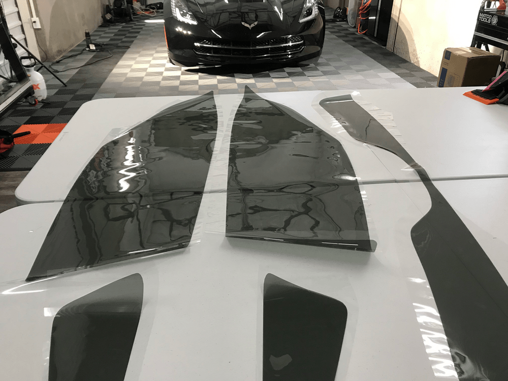 A black car is parked in a garage next to a table with pieces of a car on it.