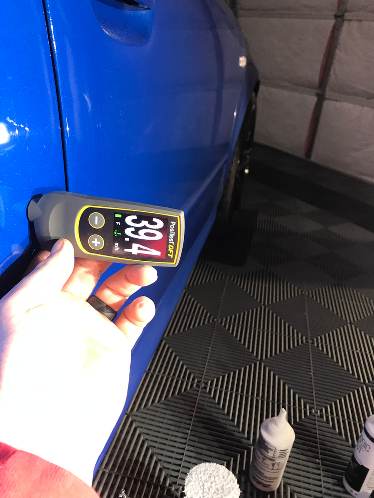 A person is measuring the thickness of a blue car