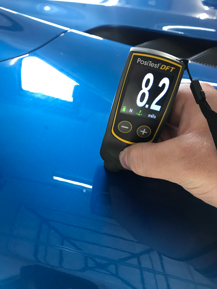 A person is measuring the thickness of a blue car