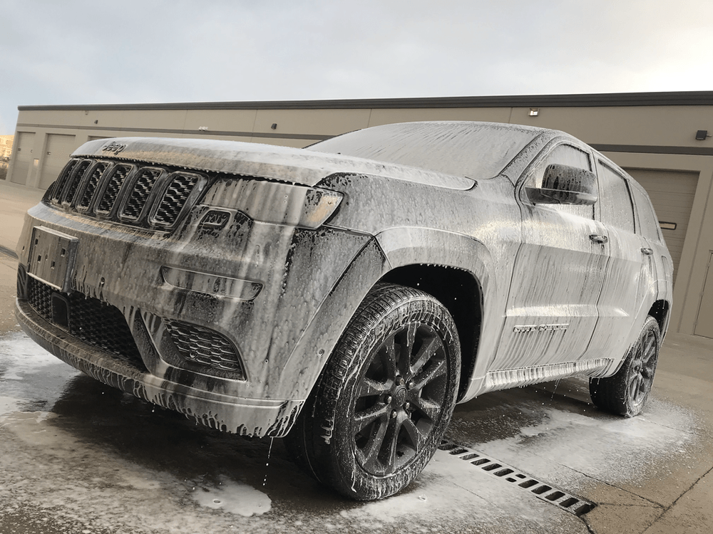 A jeep grand cherokee is covered in foam in a parking lot.