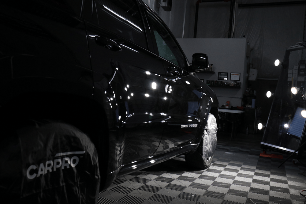 A black car is parked on a checkered floor in a garage.