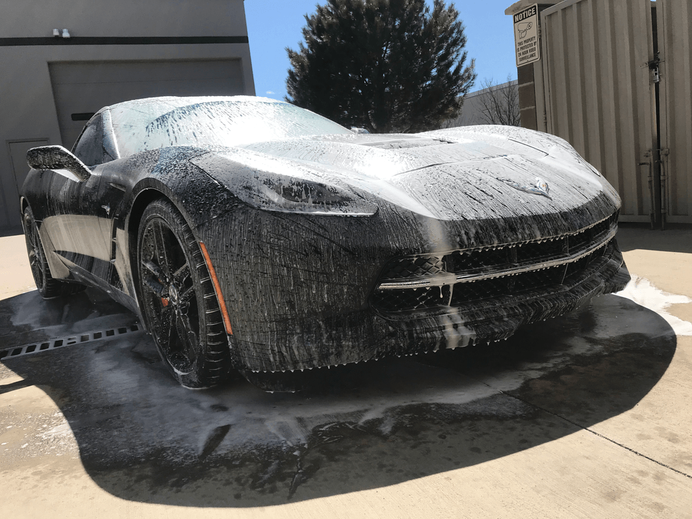 A black sports car is covered in foam in a parking lot.