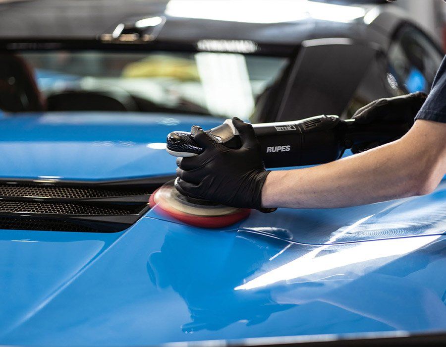 A person is polishing the hood of a blue car.