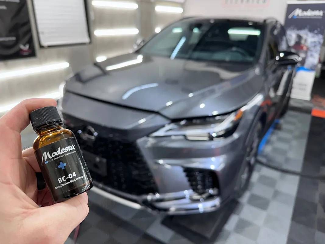A person is holding a bottle of wax in front of a car.