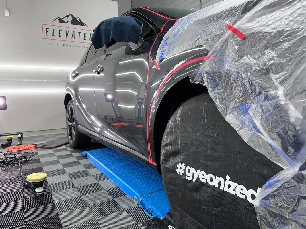 A car is sitting on a lift in a garage covered in plastic.
