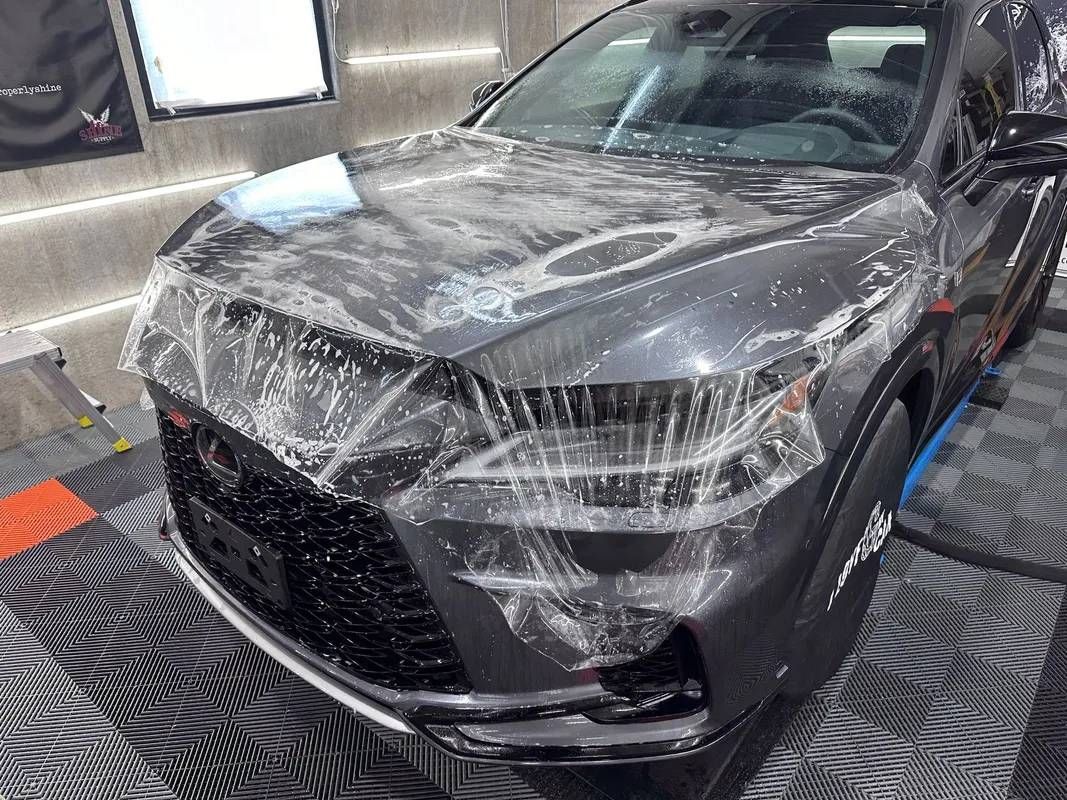 A black car is covered in plastic wrap in a garage.