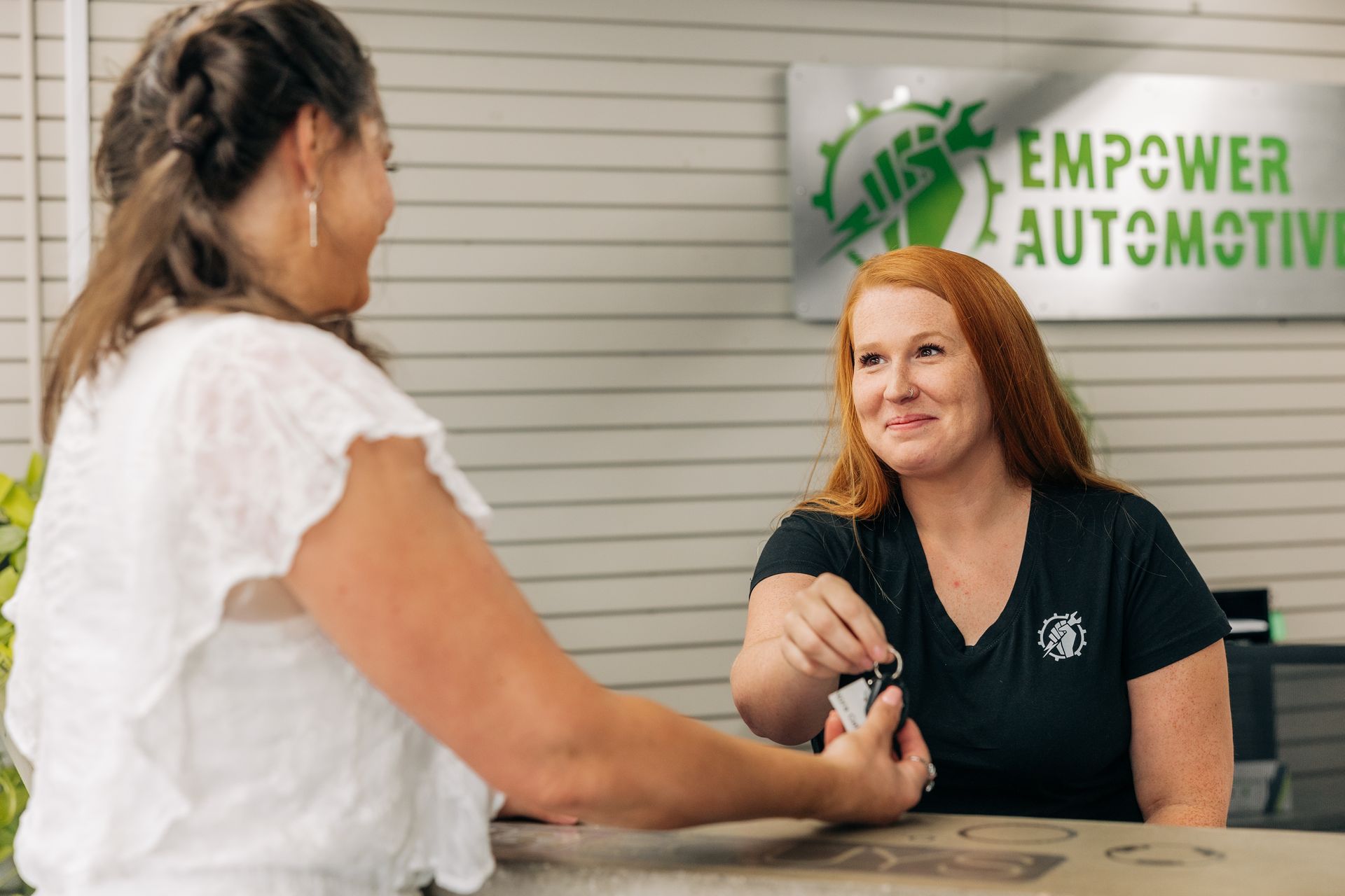 Woman handing keys to a customer at the Empower Automotive reception desk. | Empower Automotive