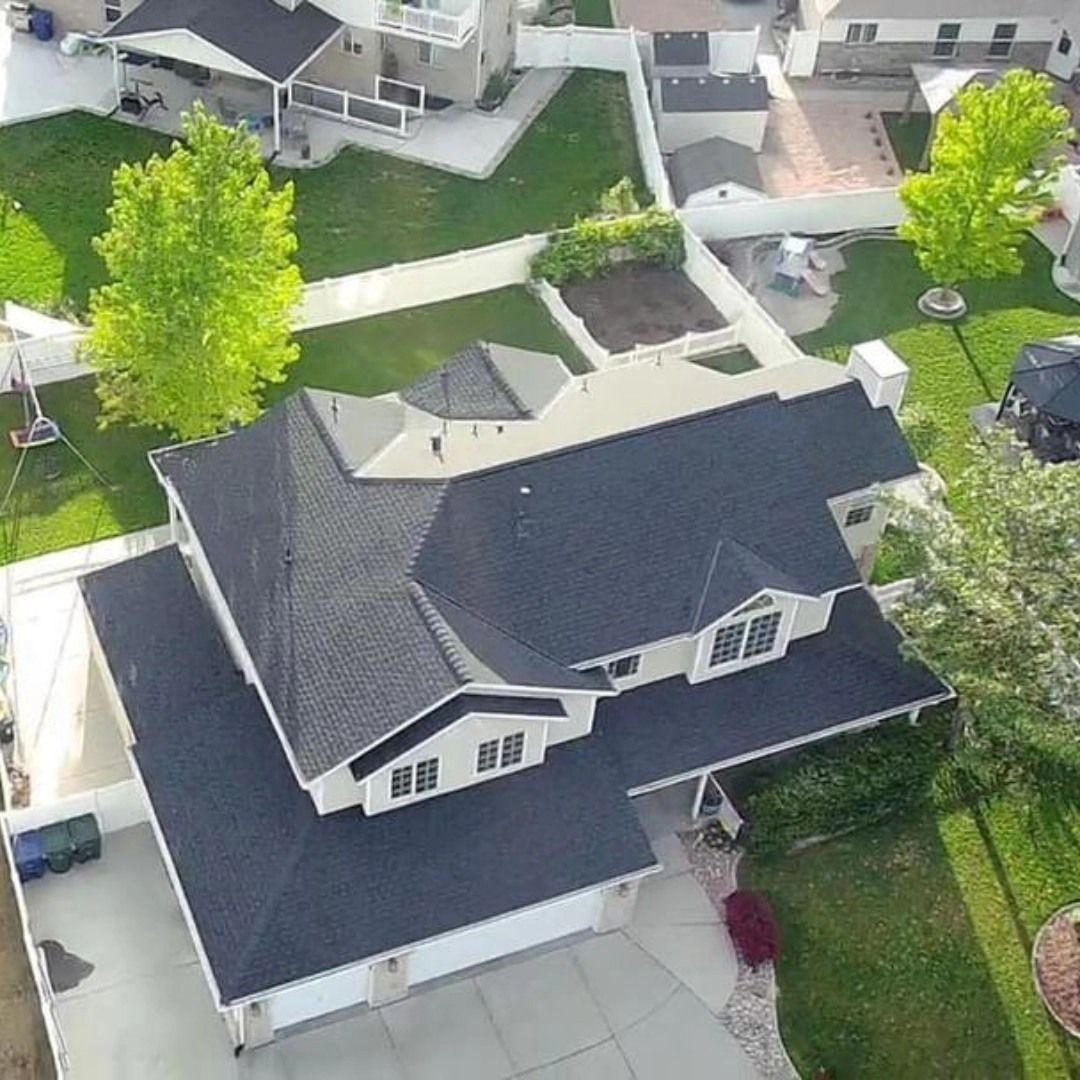 An aerial view of a large house with a black roof in a residential area.