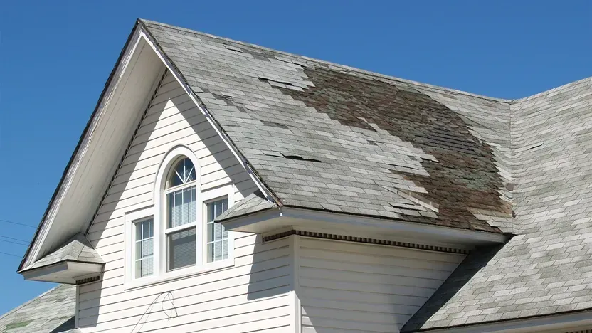 A white house with a roof that is missing shingles