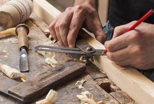 hand of a carpenter taking measurement of a wooden plank