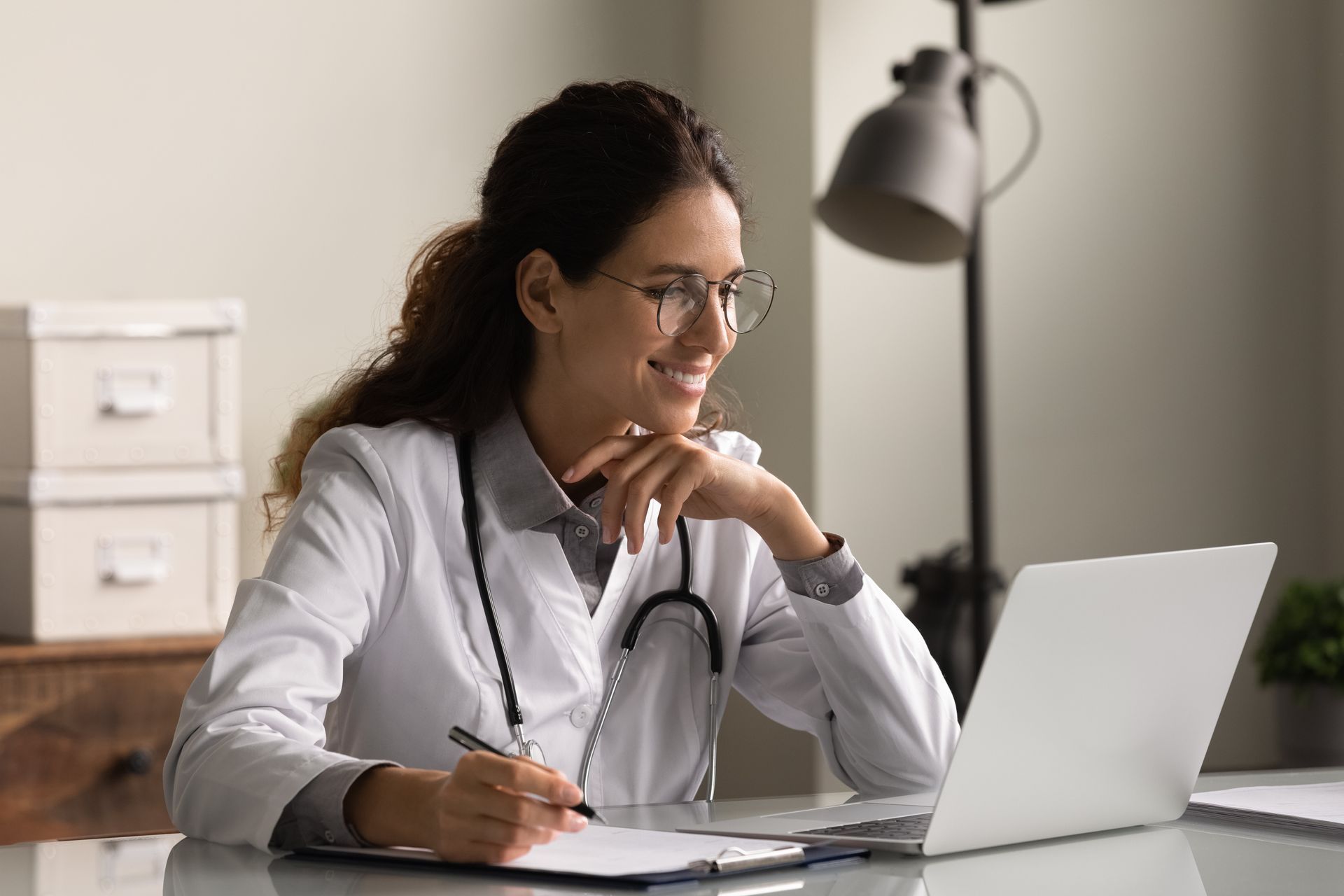 Medical professional writing notes at a laptop. Medical professional writing notes at a laptop.