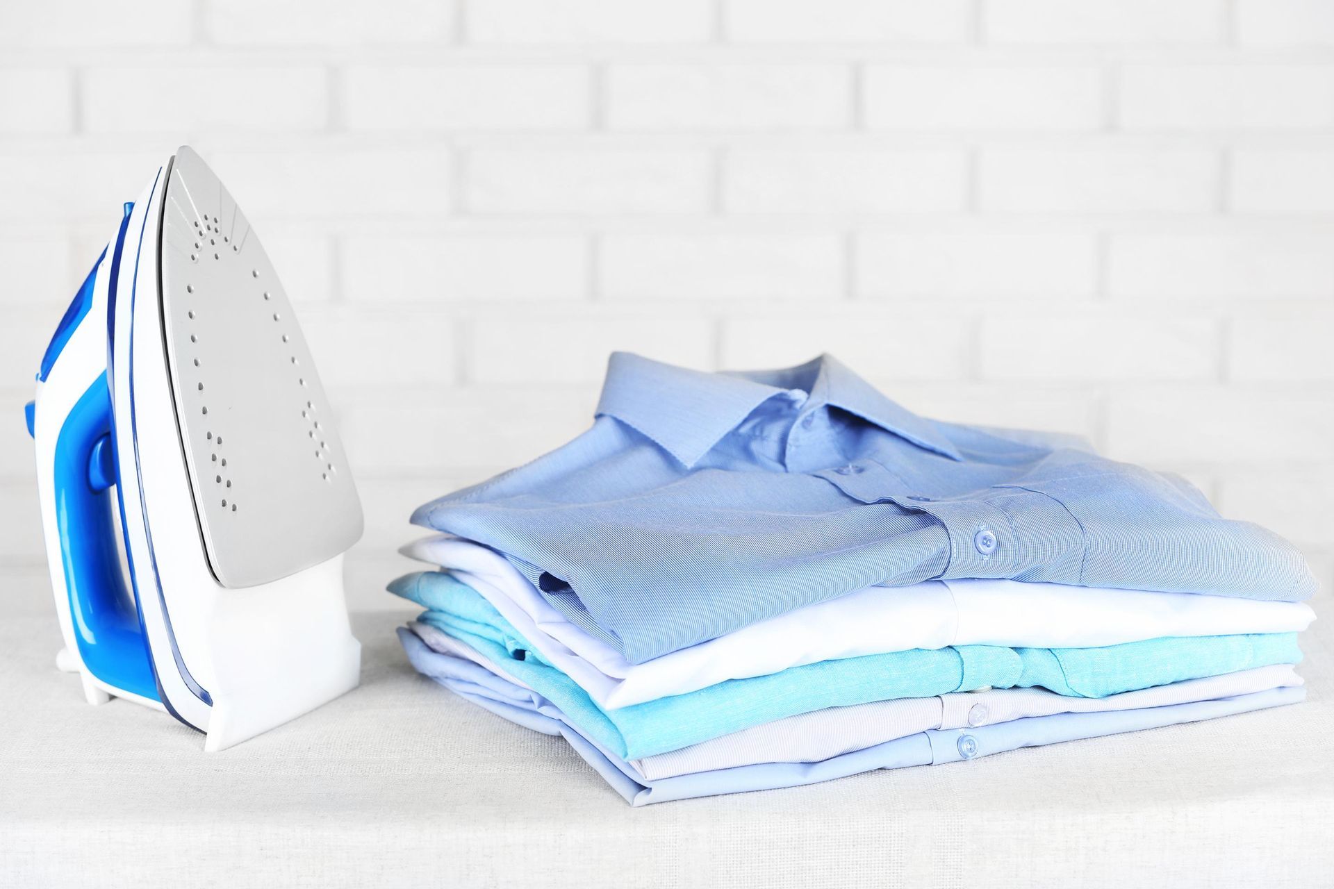 a stack of shirts next to an iron on a table
