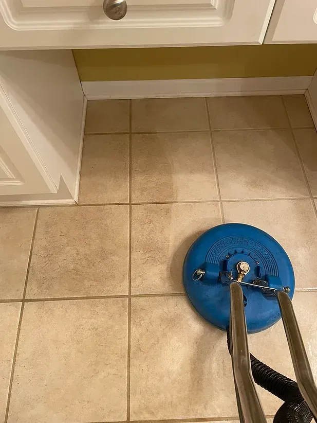 Blue floor-cleaning machine on tan tile kitchen floor beneath white cabinets