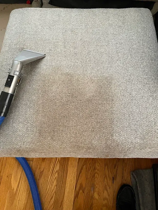 Beige upholstered cushion with a dirty brown stain in the center, next to a handheld tool handle.