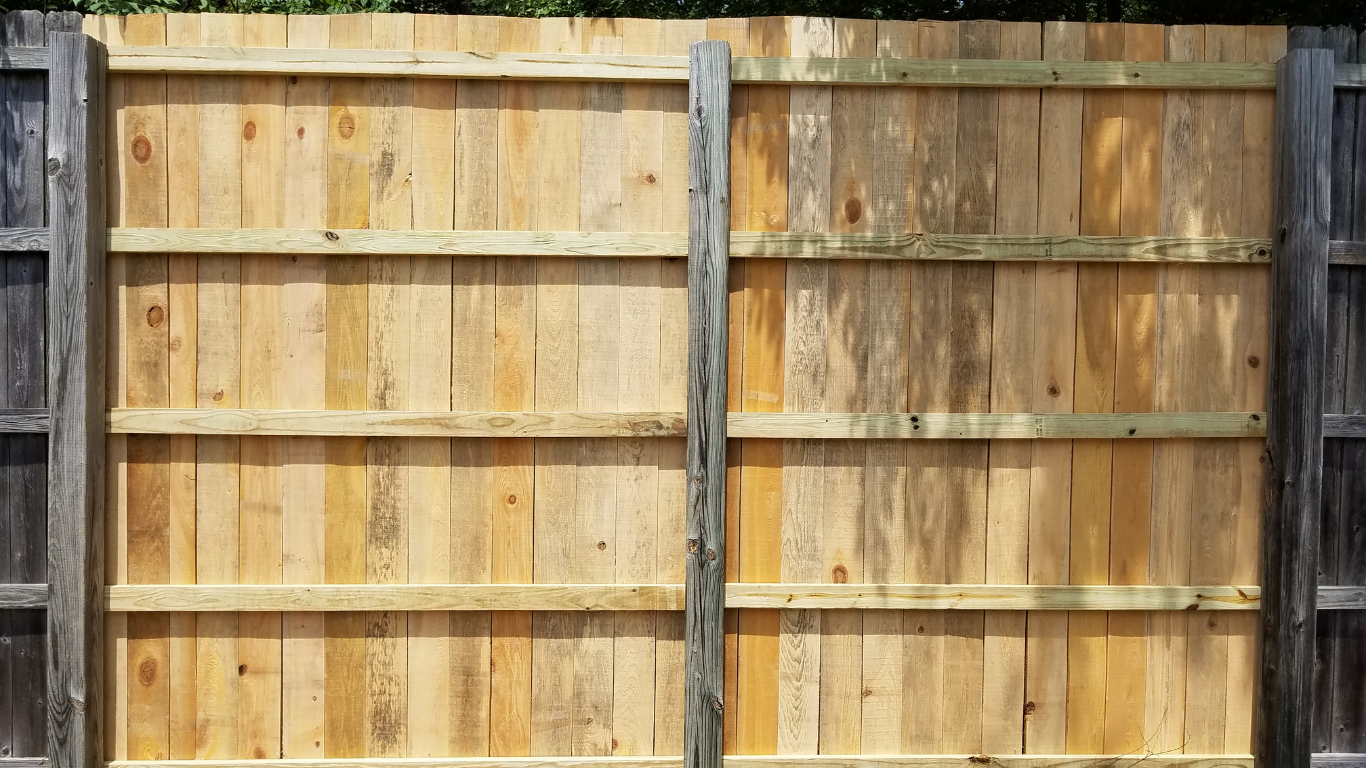 Wooden fence with horizontal supports, weathered wood on the right, new wood on the left, dark posts.