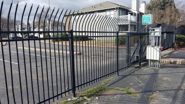 Black metal fence in front of apartment buildings on a sunny day.