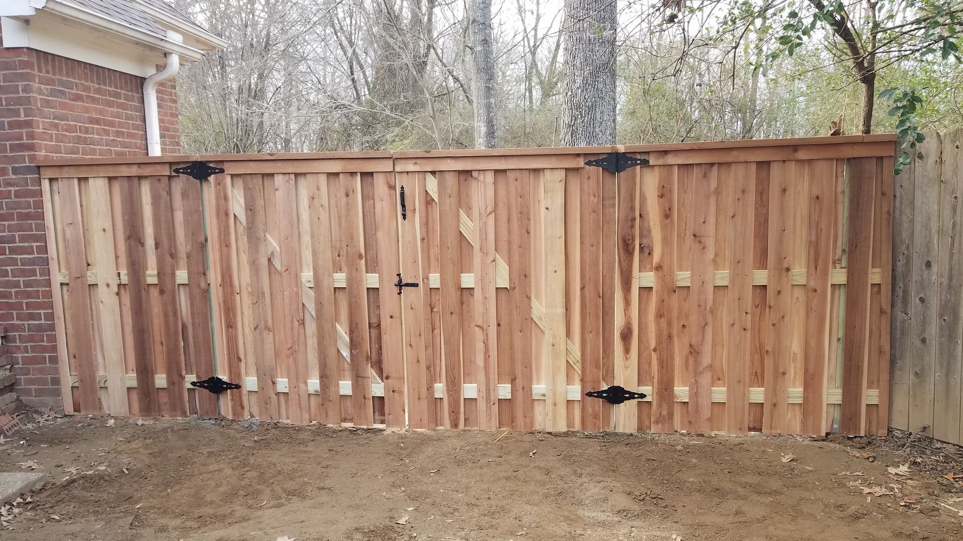 A new wooden double-gate fence section installed outdoors next to a brick building.