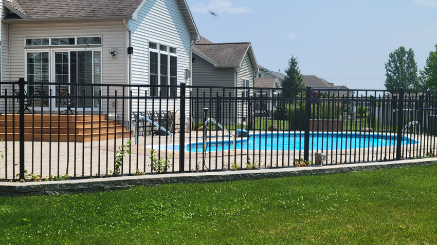 Black metal fence surrounds a blue pool in a backyard. House in background.