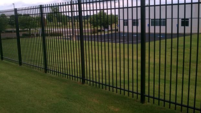 Black metal security fence on green grass in front of a building.
