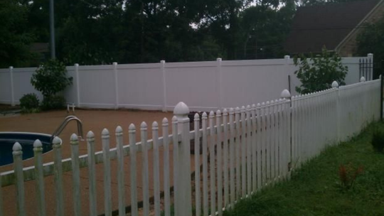 White picket fence next to a pool, with a taller white privacy fence behind it.
