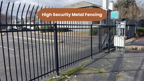 Black metal fence in front of a paved area and multi-story apartment building.