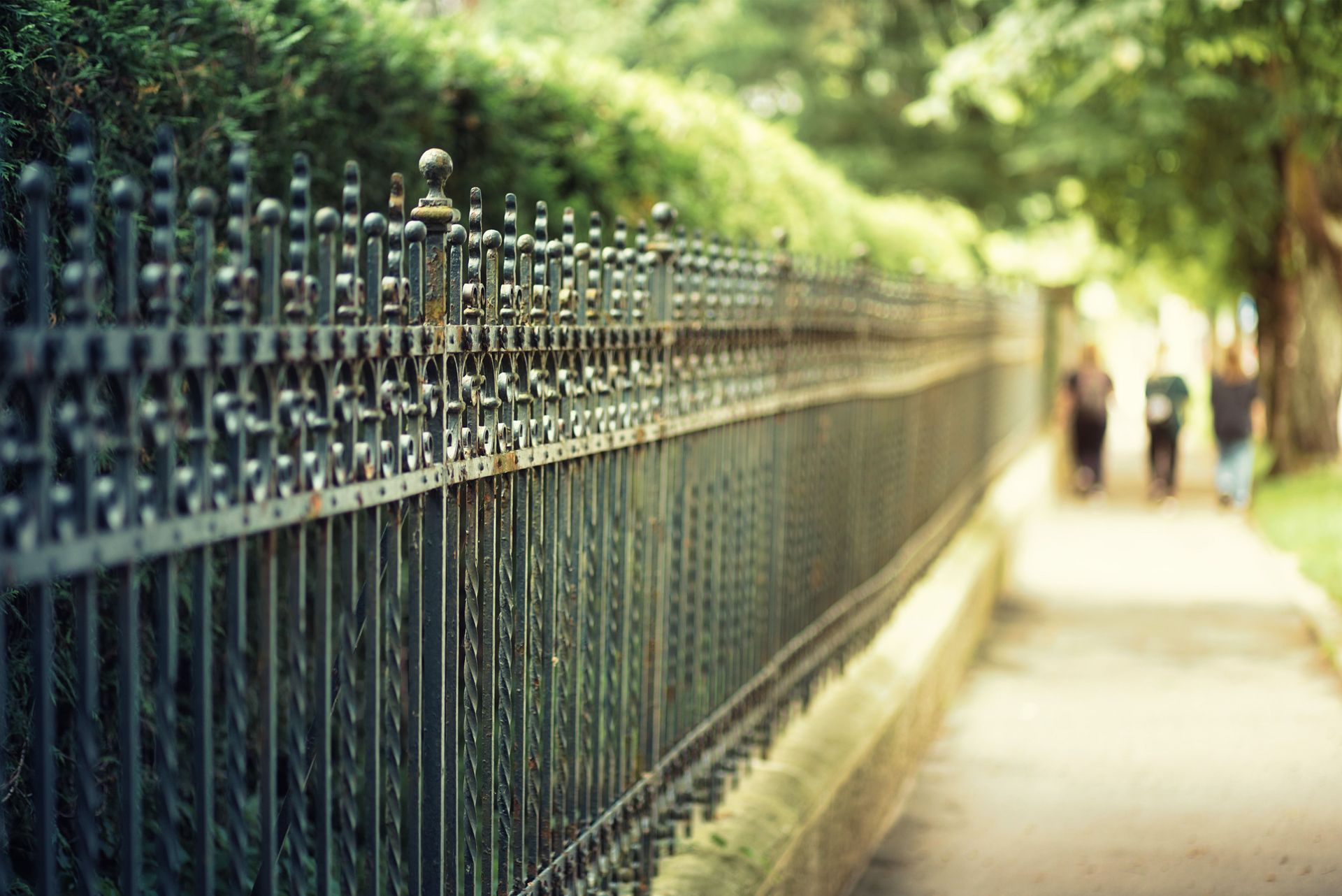 Black metal fence in front of a paved area and multi-story apartment building.