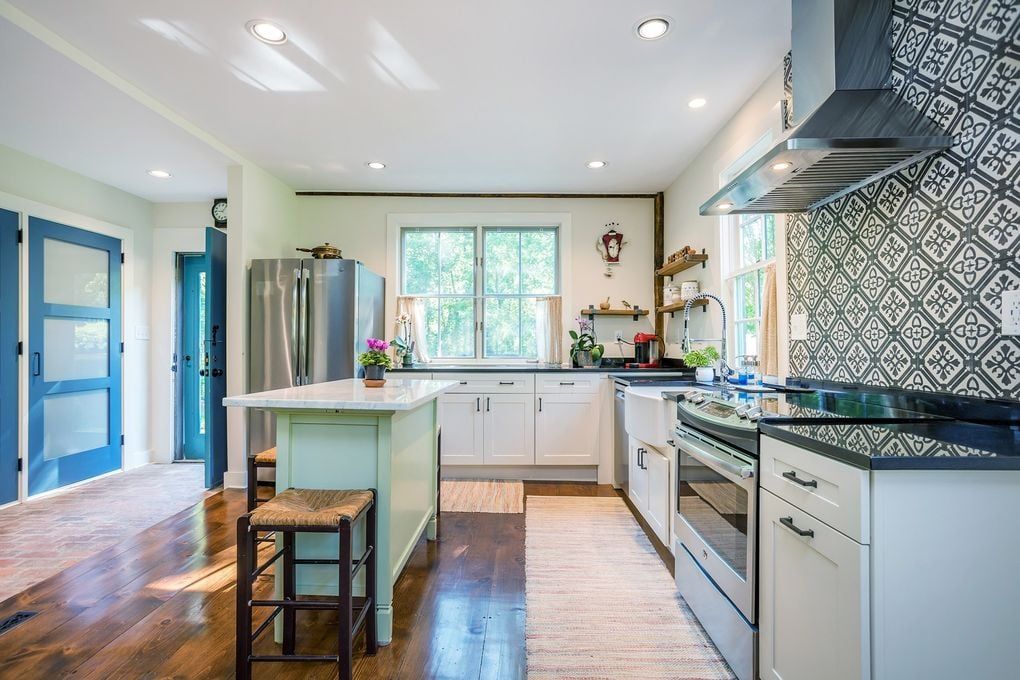 Kitchen with light green island, white cabinets, stainless steel appliances, and patterned backsplash.