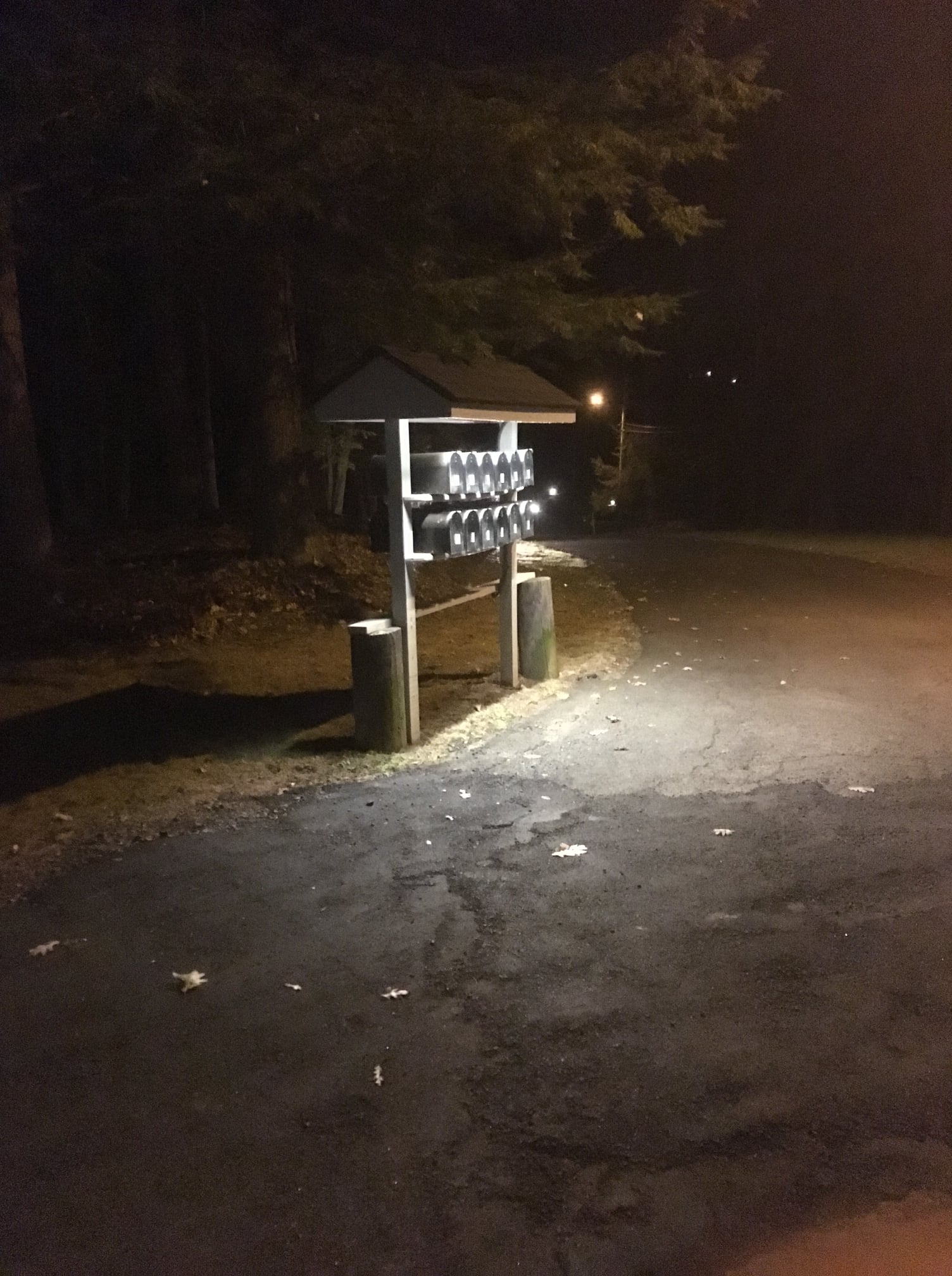 Dark view of illuminated mailboxes on a post at night, on asphalt path.