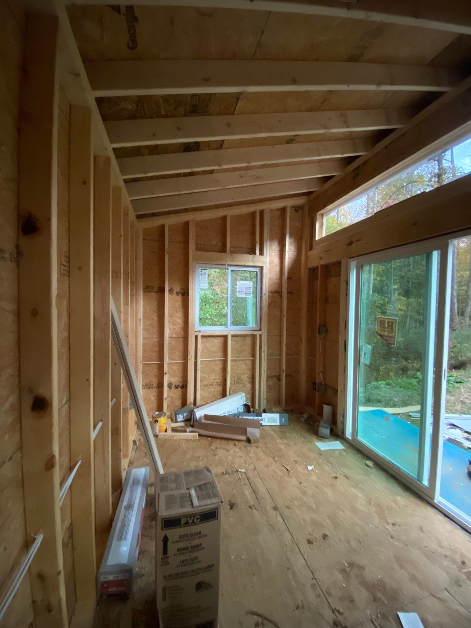 Interior of a wooden framed room under construction, with windows and a sliding glass door.