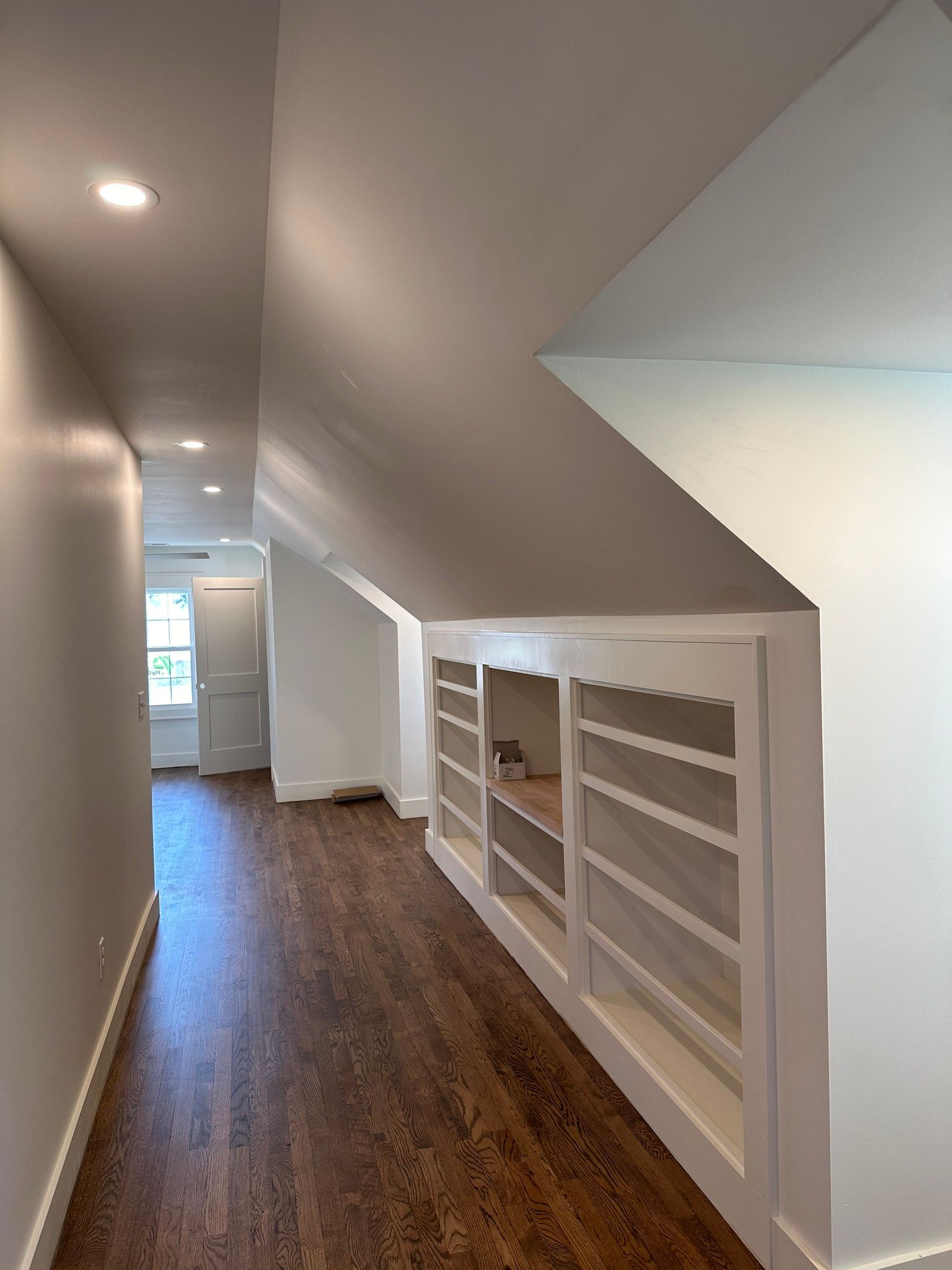 Narrow hallway with built-in white shelves and wood floors. Recessed lighting in the ceiling.