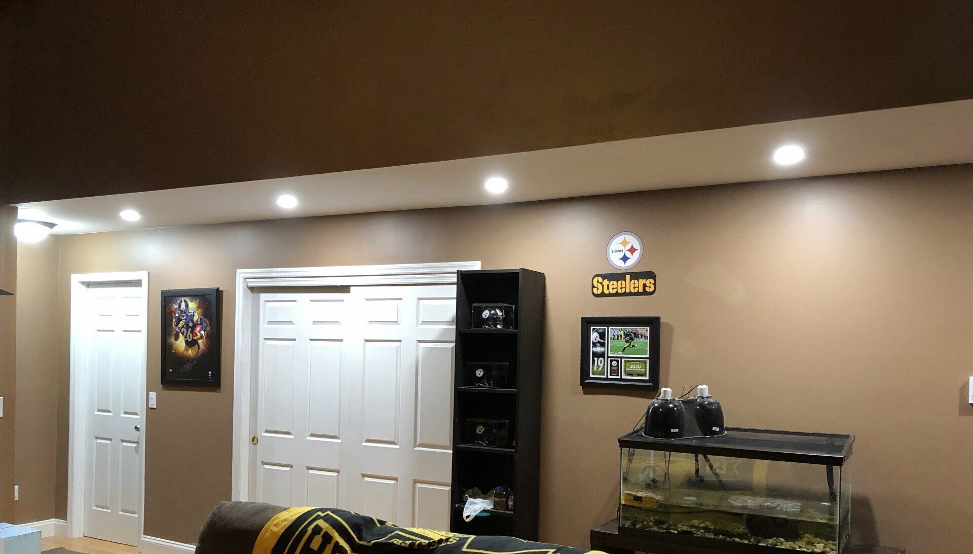 A basement with a fish tank, Steelers decor, a closet, and built-in lighting.