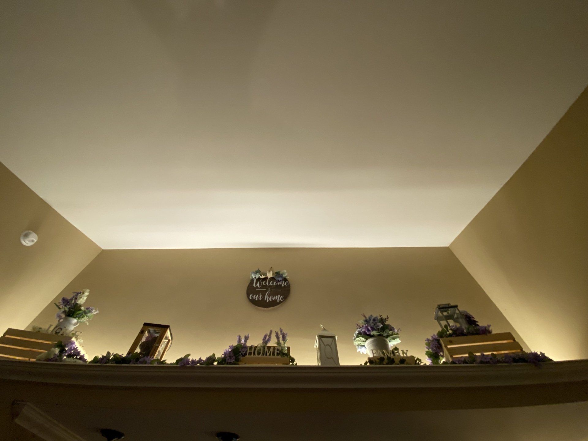 Shelf with decorations: florals, clock, and picture frames; against a beige wall, under a white ceiling.