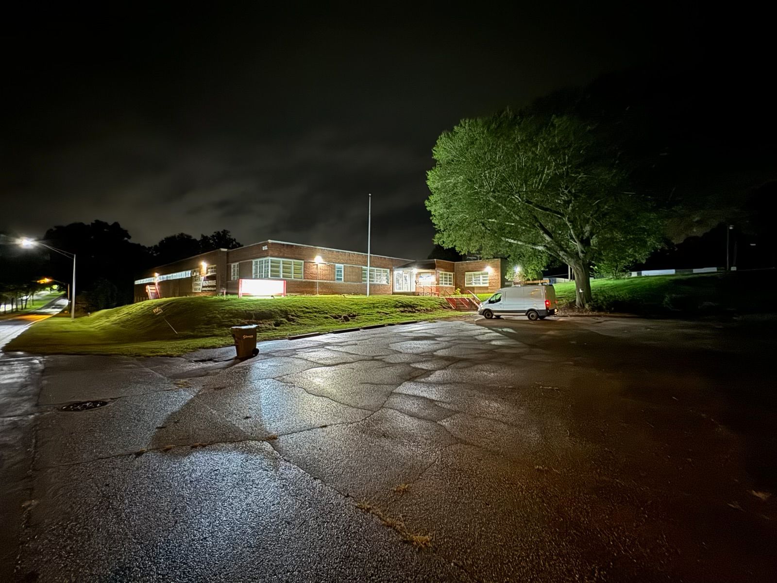 Brick building at night, wet asphalt, tree on right, cloudy sky, street lights.