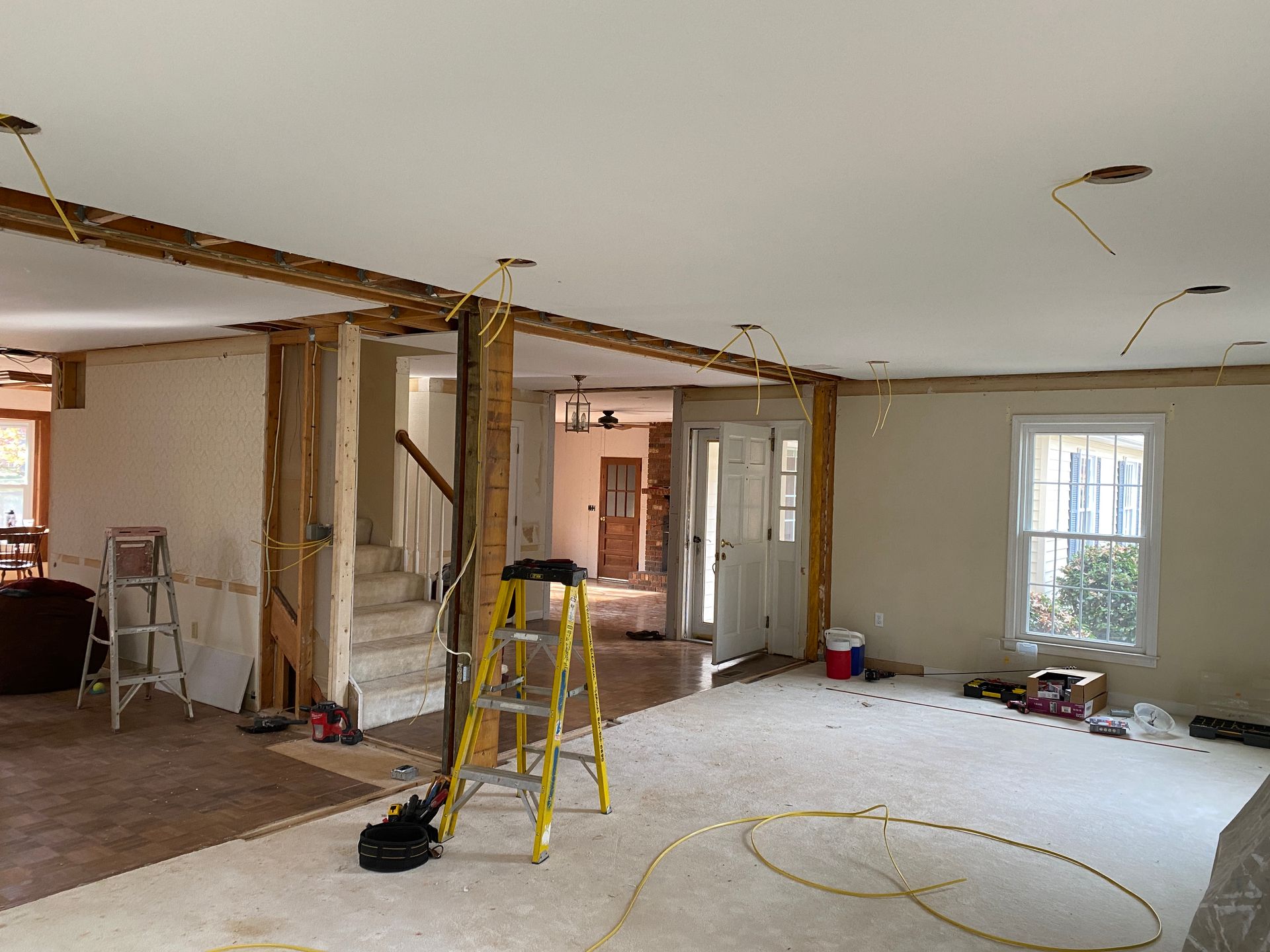 Room renovation with exposed beams, wiring, and a ladder.
