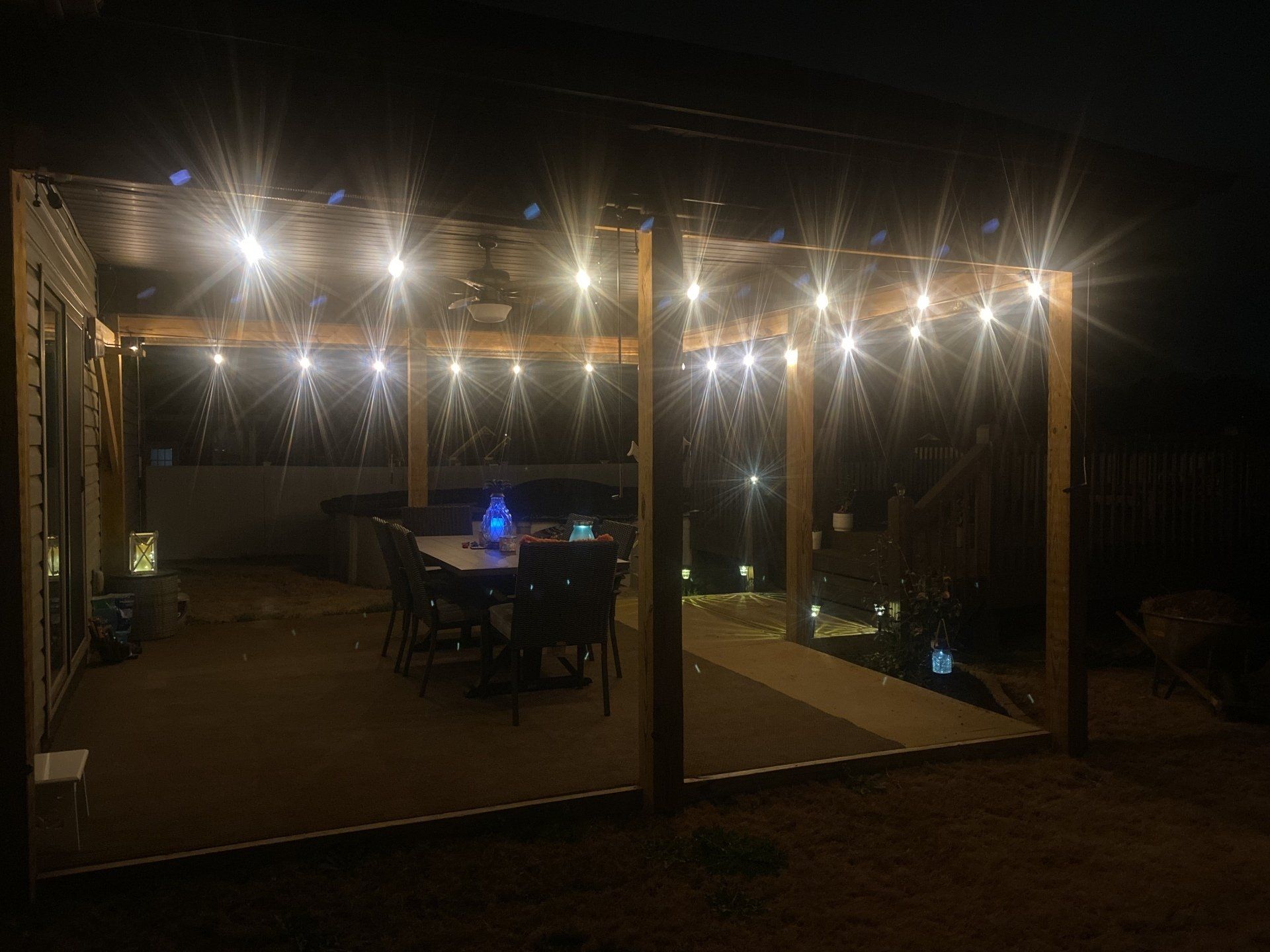 Patio with string lights illuminating a dining table and wooden pergola at night.