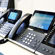 A row of modern black VoIP office desk phones with touchscreens and numeric keypads arranged on a white surface.