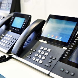 A row of modern black VoIP office desk phones with touchscreens and numeric keypads arranged on a white surface.