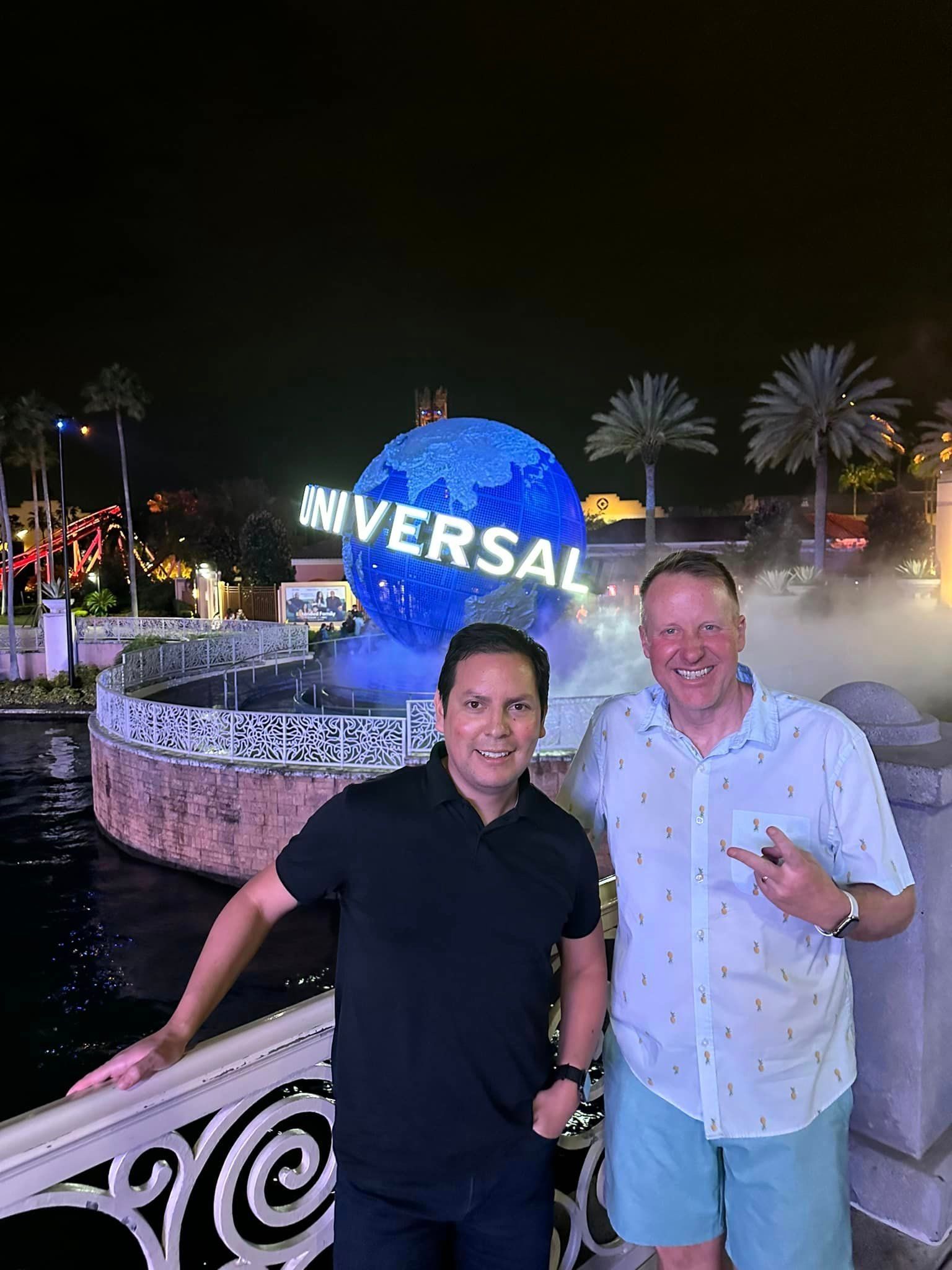 Two men are standing next to each other in front of a universal studios globe.