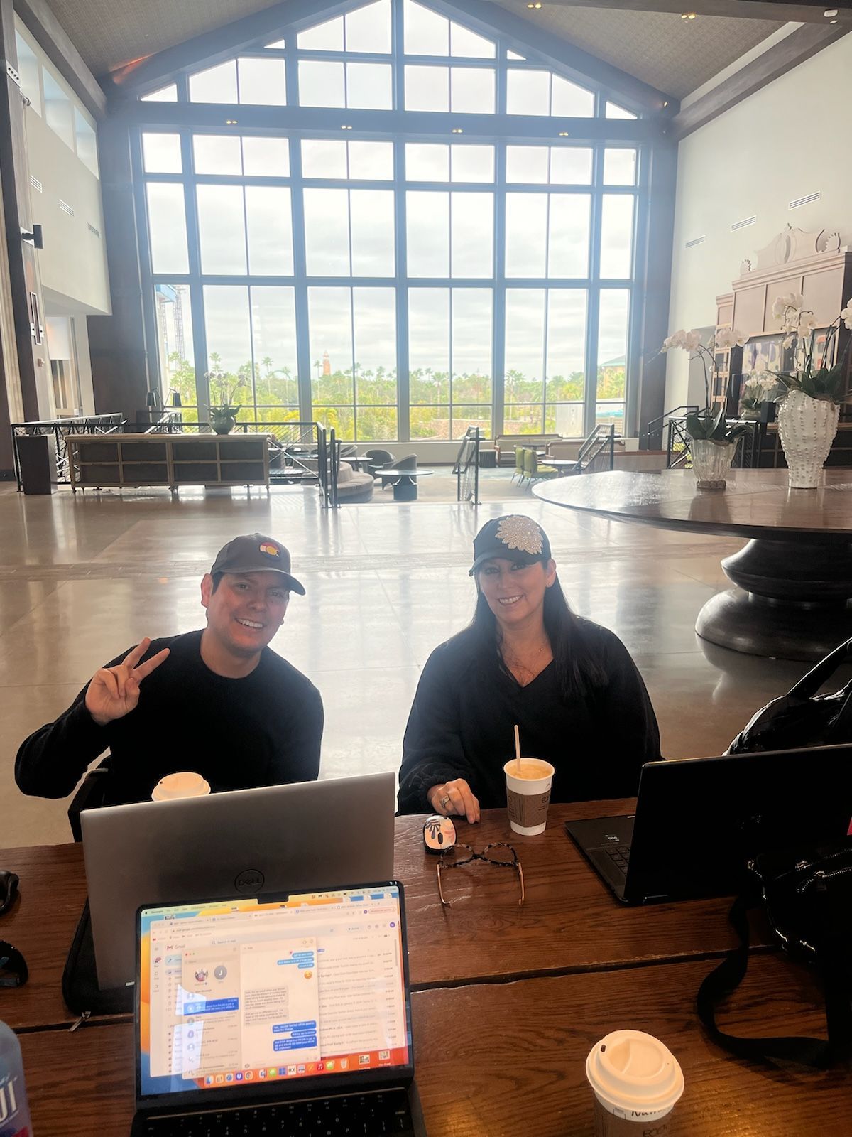 Two people are sitting at a table with laptops in front of a large window.