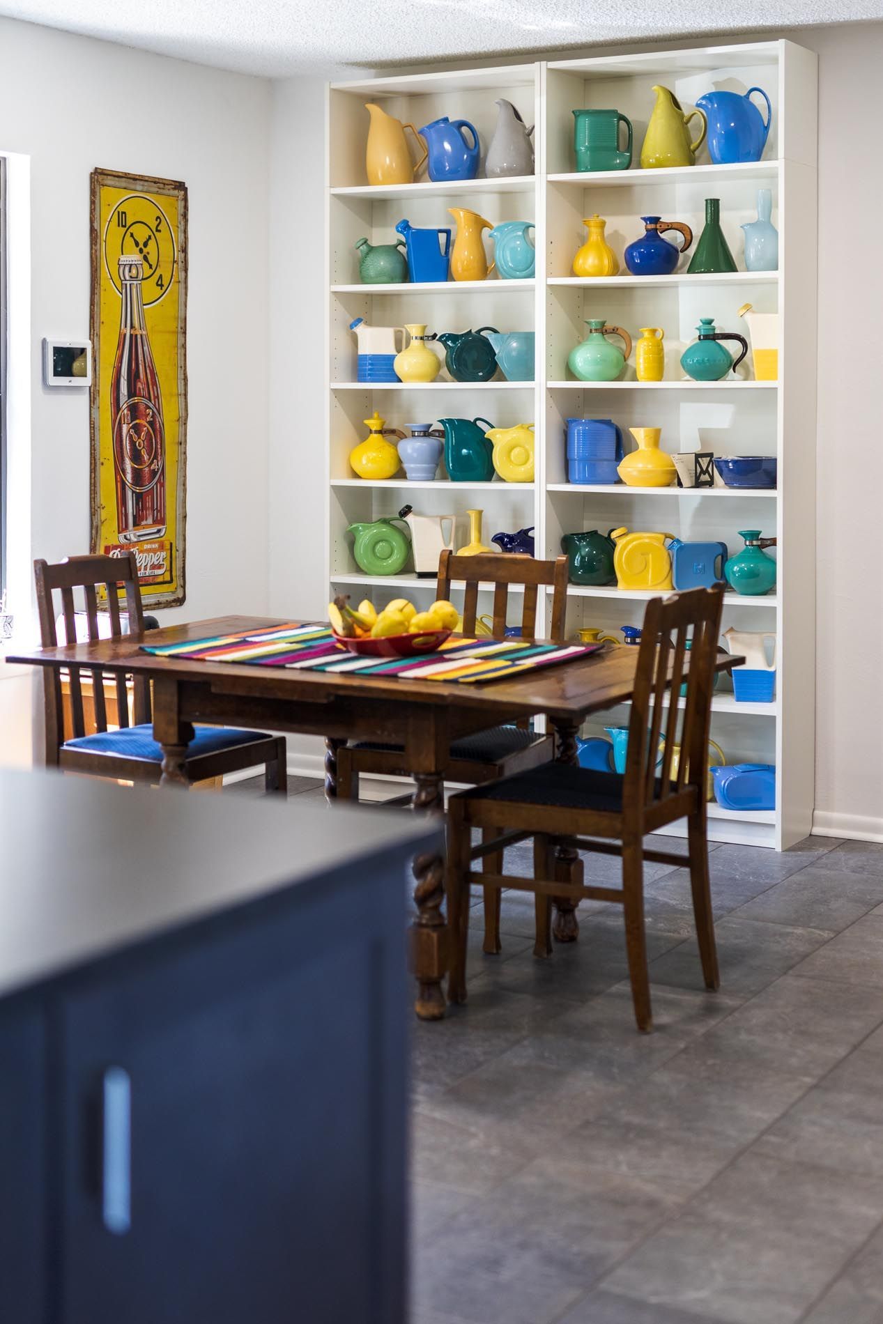 Dining room with wooden table, chairs, and built-in shelves filled with colorful pottery.