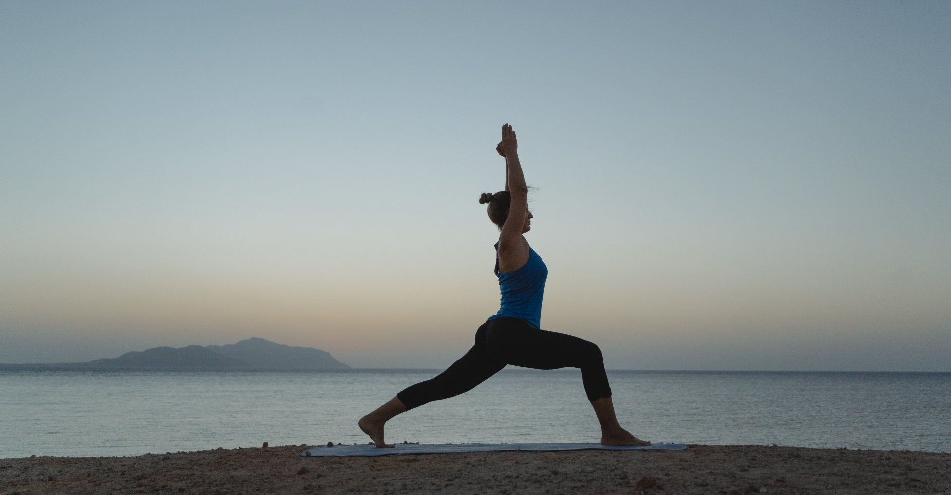 A woman is practicing yoga on the beach at sunset.