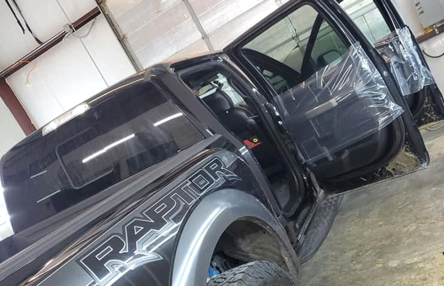 Black Ford Ranger pickup with open door, parked inside a garage with a wet floor.